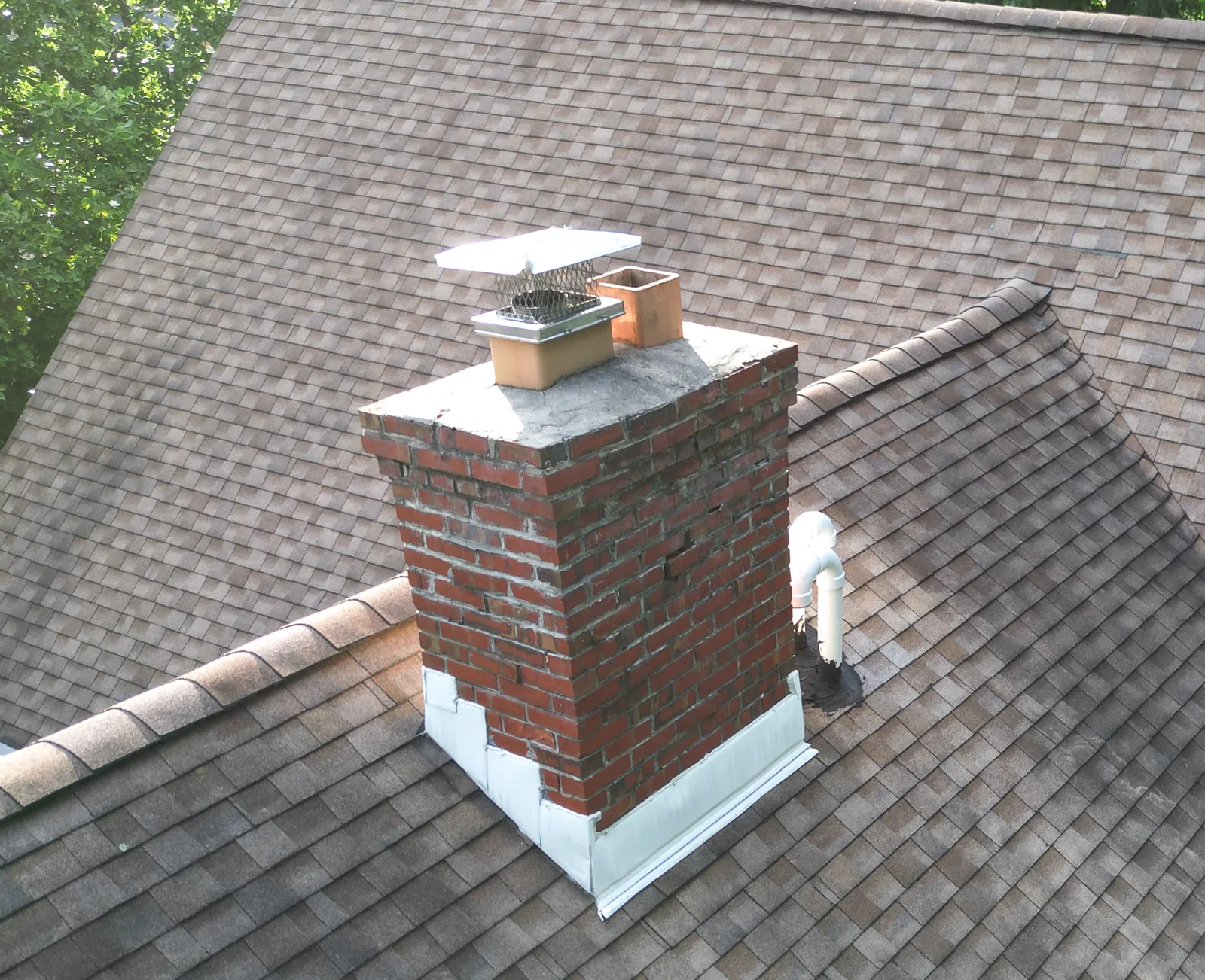 Close-up aerial inspection photo of a brick chimney, cap, and asphalt shingle roof