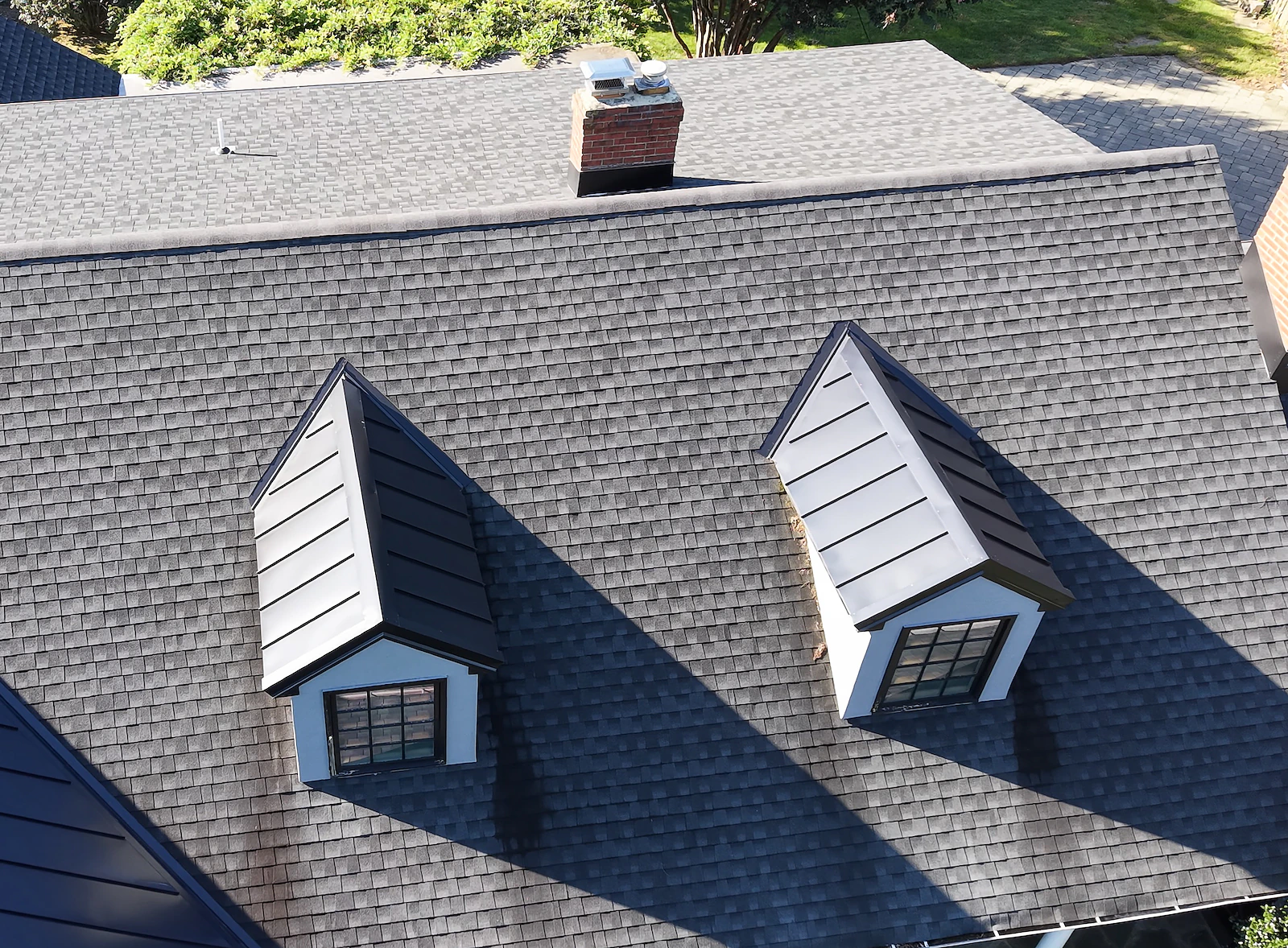 Close-up aerial documentation of dormer windows, chimney and asphalt shingles on a residential roof