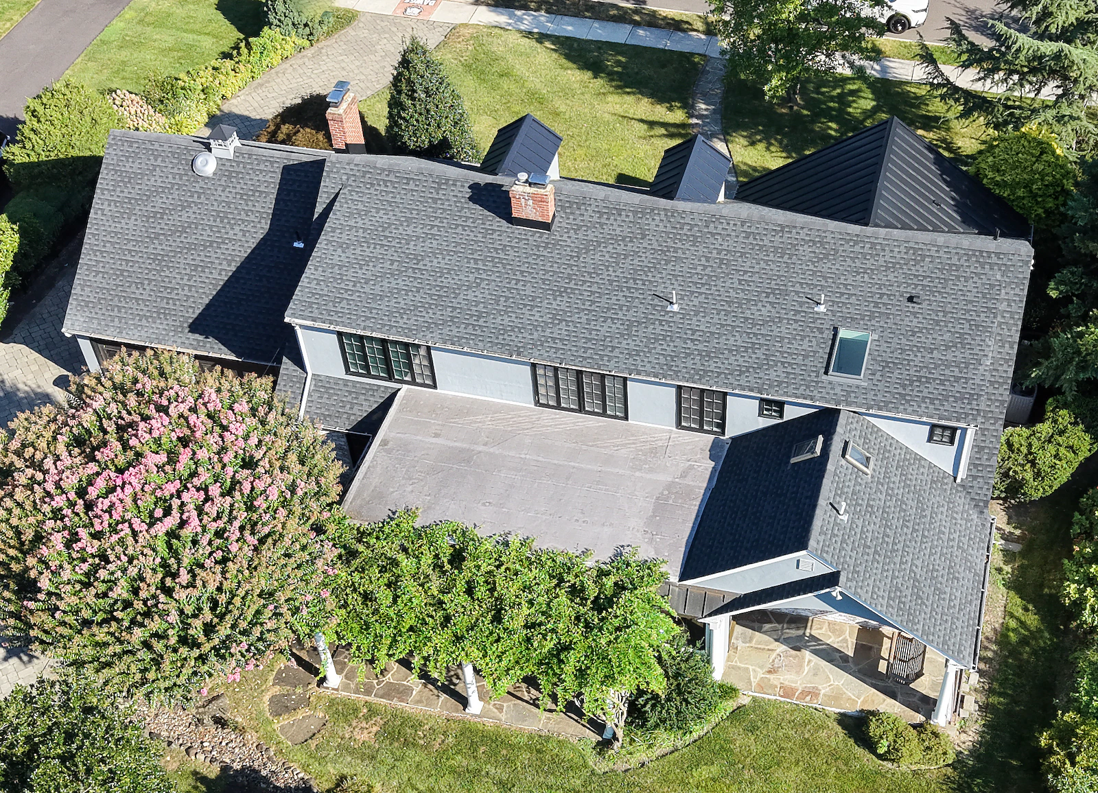 Aerial view of a slate-roof colonial home showing the front elevation, entry courtyard and paver driveway