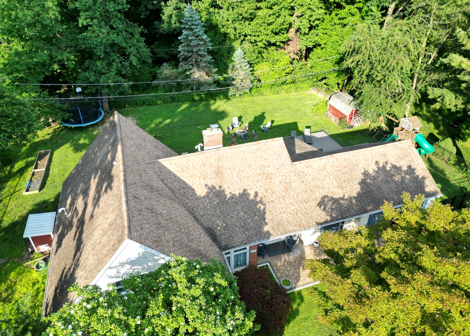 Low-altitude aerial drone photo showing a home's roofline, backyard, and landscaping
