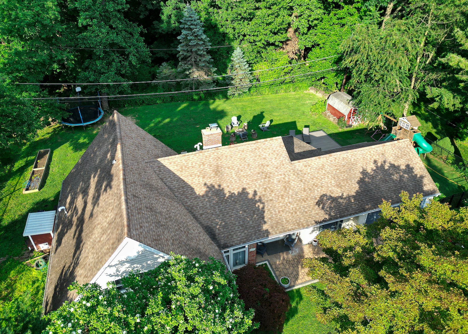 Aerial view of a single-story ranch home with a shingle roof, large lawn and mature trees